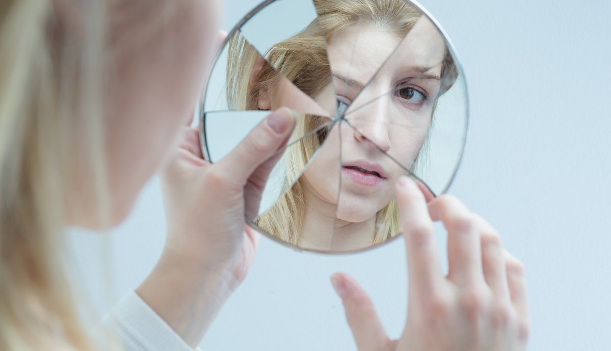 Woman peers at reflection in a broken mirror.