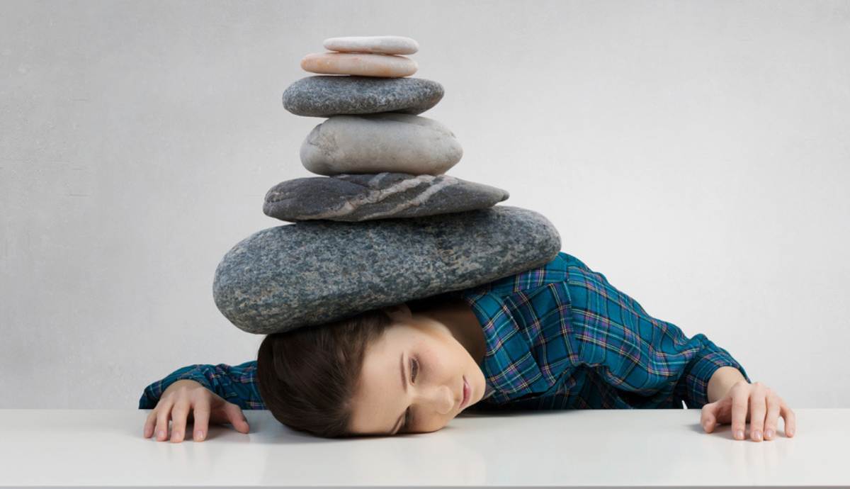 woman pressed flat on table with stones stacked on her back.