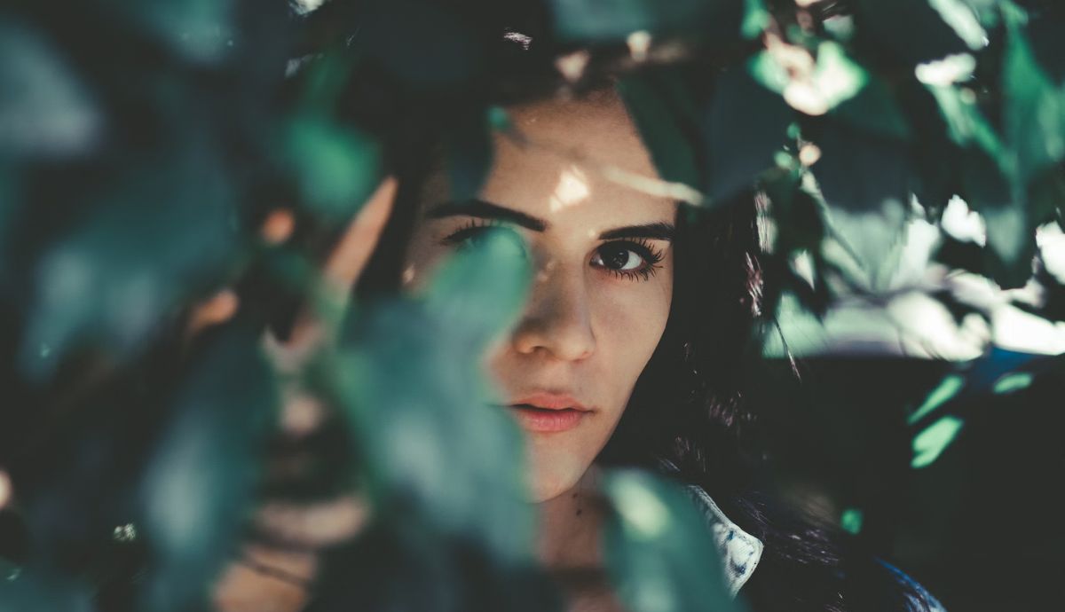 young woman peering from behind shrubbery