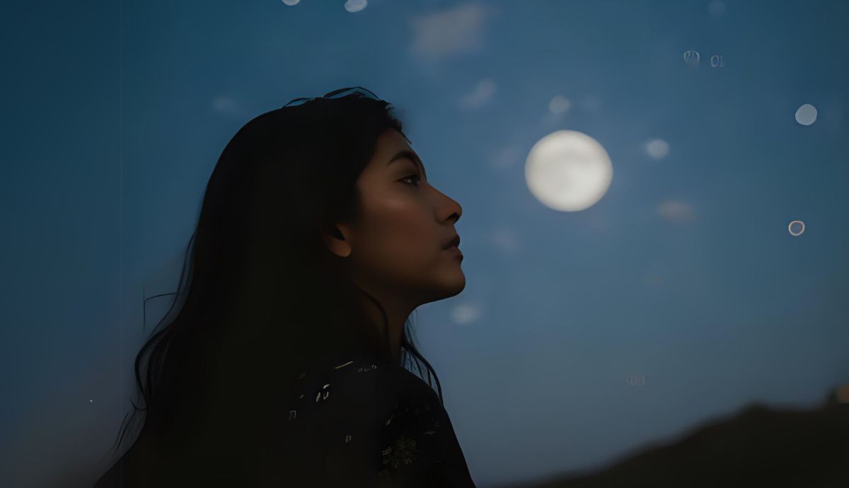 Young woman gazes up at the sky with a full moon looming in the background.